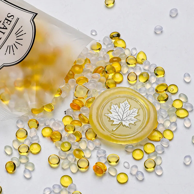 A pile of clear and yellow wax sealing beads scattered on a white surface next to a plastic container.