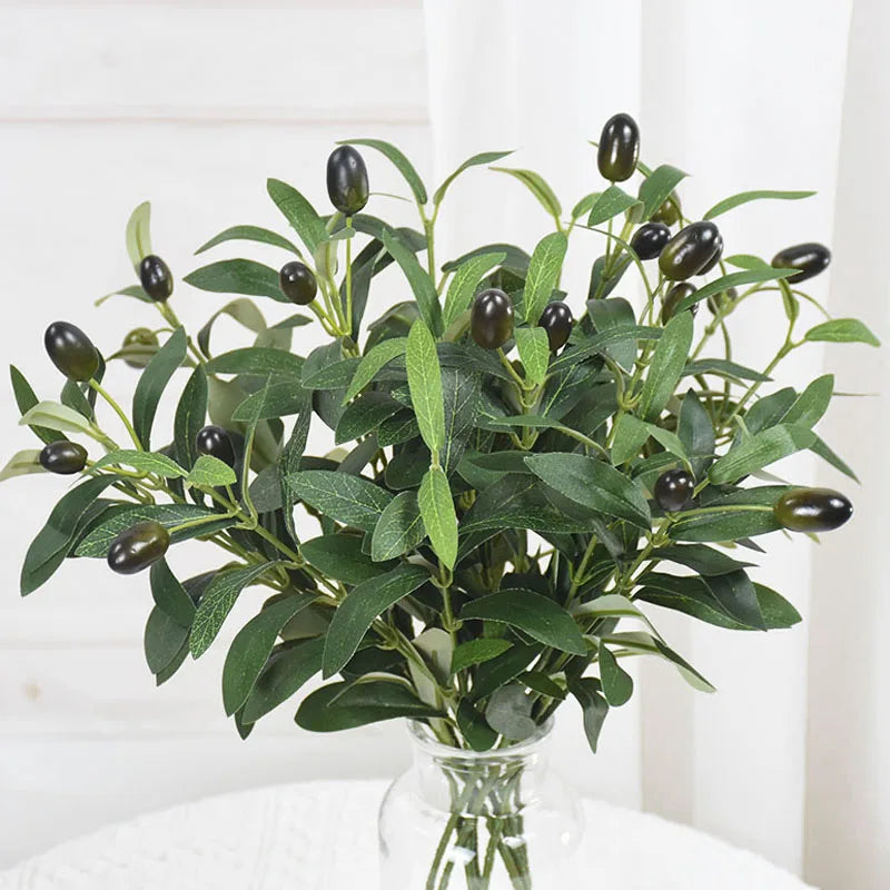 Artificial olive leaf branch with dark green leaves and small berries displayed in a clear glass vase.