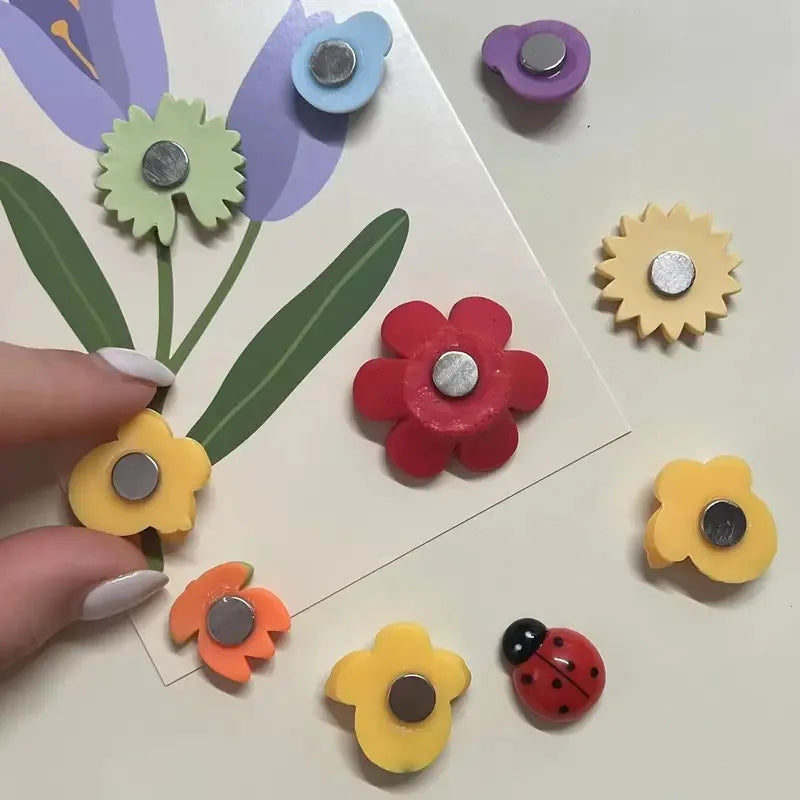 A collection of colorful, reusable fridge magnets shaped like flowers and insects on a white background.