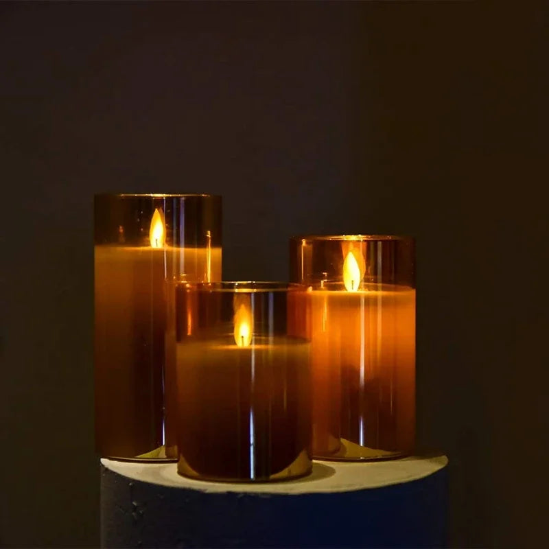 Three amber glass pillar candles are lit on a light blue surface against a dark background.