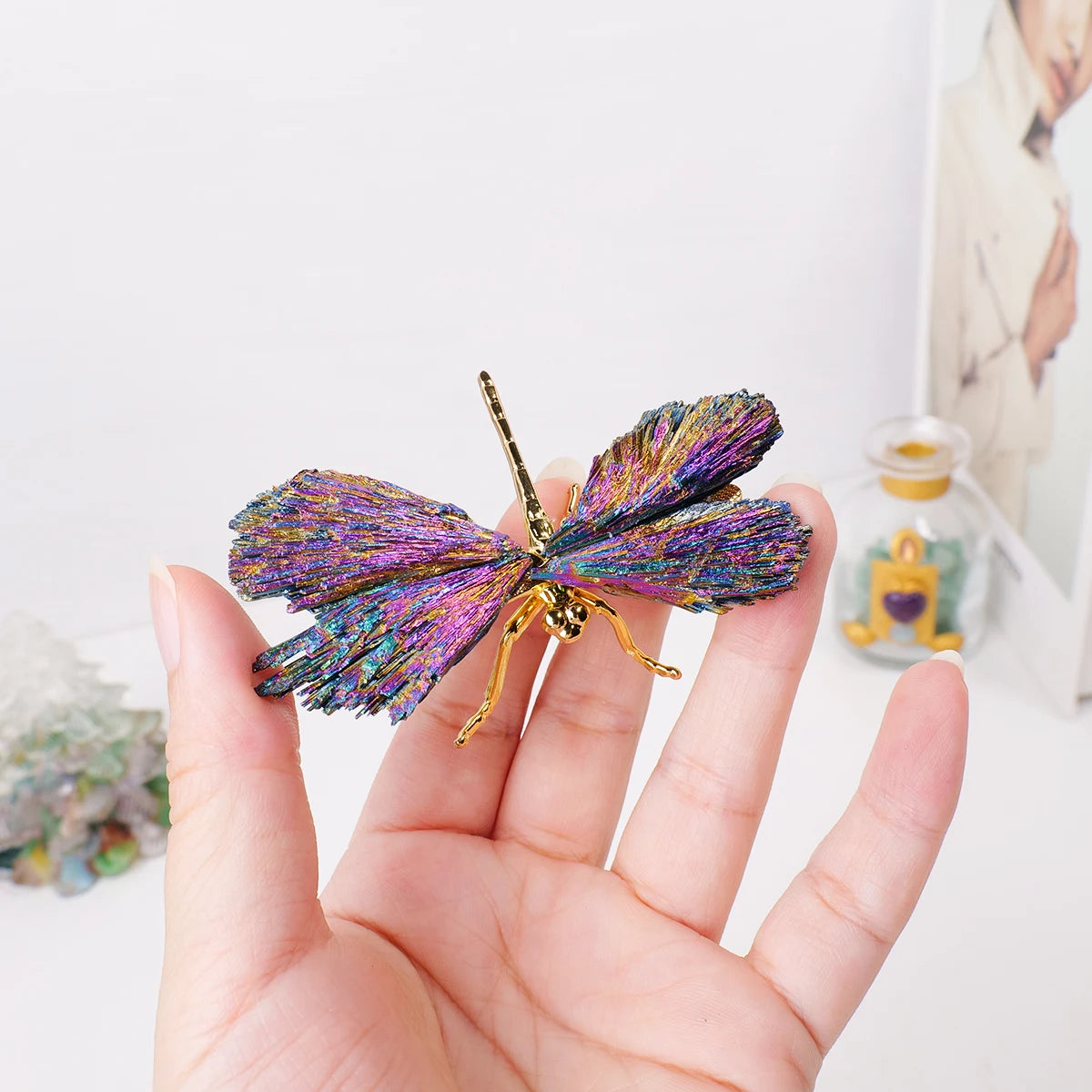 A hand holds a natural crystal tourmaline dragonfly figurine with iridescent purple and blue wings.