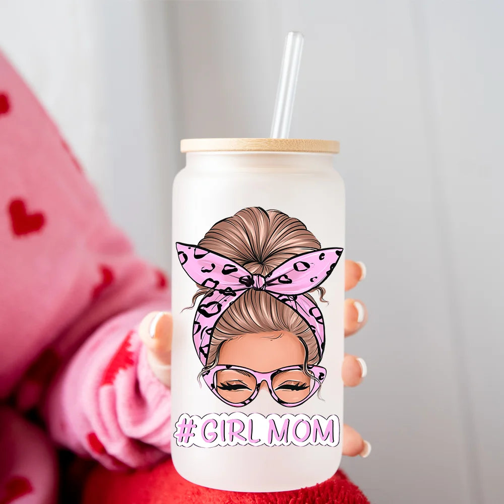 A hand holds a clear tumbler featuring a drawing of a woman with her hair tied up in a bow and wearing glasses, with the text