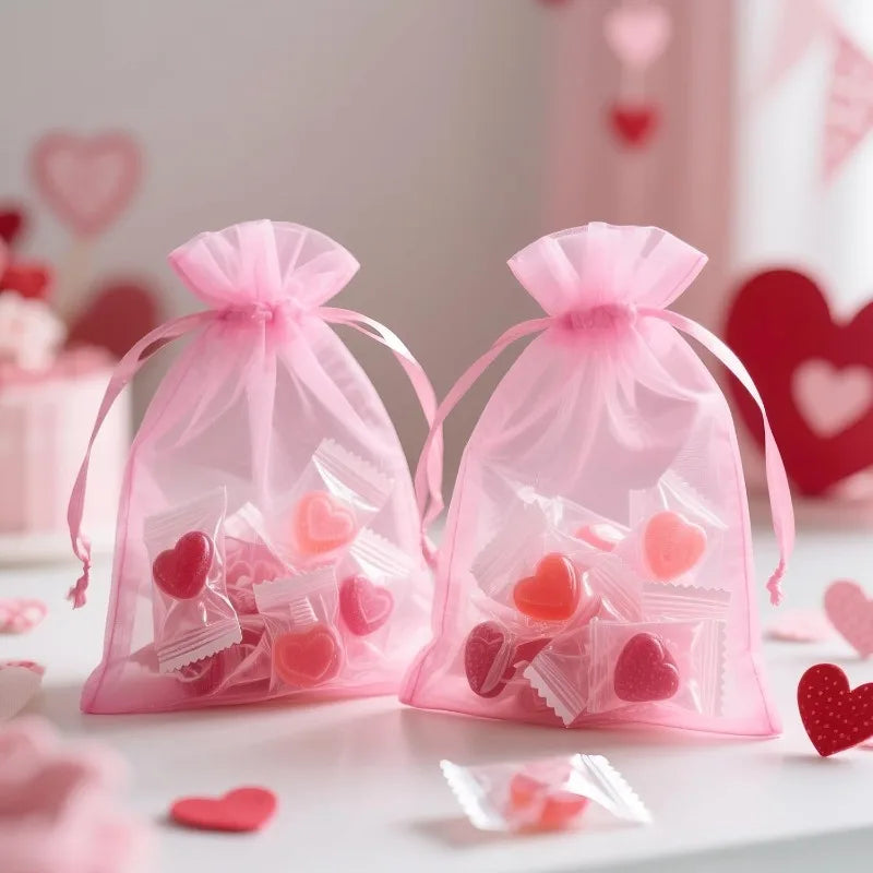 Two pink organza drawstring bags filled with heart-shaped confetti and small candies