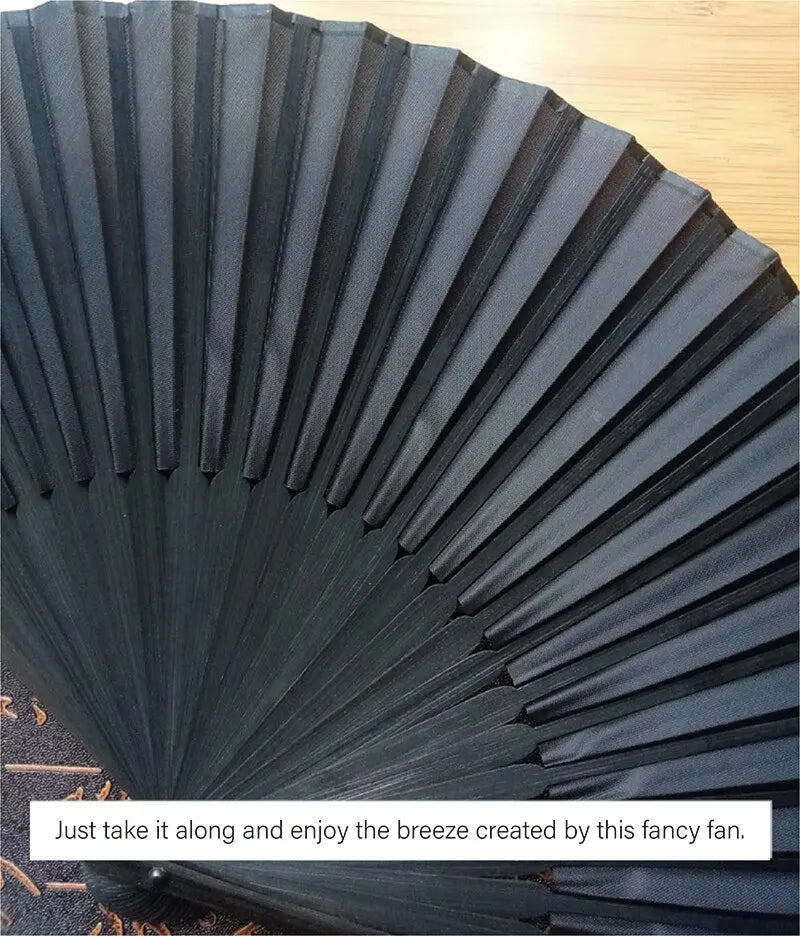A close-up of a black folding hand fan with bamboo ribs, showing the pleated surface and texture.