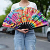 A person holds a vibrant UV fluorescent handheld folding fan with colorful floral patterns.