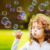 A young child is blowing bubbles with a heart-shaped bubble wand outdoors.