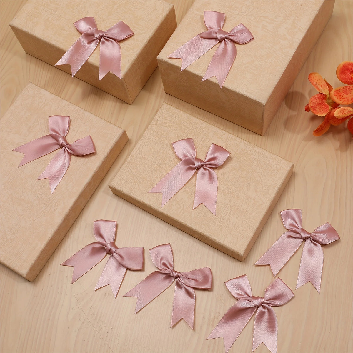 A collection of pink satin ribbon bows are displayed on light brown gift boxes.