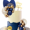 A tiered cake decorated with blue and gold spherical balls and large blue feathers, set against a white background.