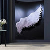 A tapestry wall hanging depicting a large white angel wing against a dark background.