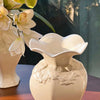 A white ceramic vase with a sculpted floral relief detail holds a white orchid flower.