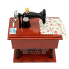 A vintage sewing machine music box with a black body and brass accents resting on a wooden base.