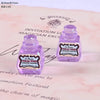 Two small purple resin potion bottles with labels are displayed on a pink paper background.