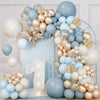 A large arrangement of latex balloons in blue, sand, white, and gold forming a wreath or floral display.