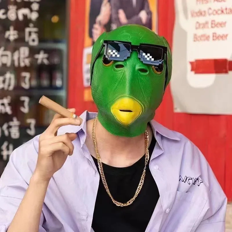 A person wearing a realistic green horror mask with black sunglasses and a purple shirt, holding a cigarette.