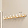 A walnut wood coat rack with eight white hooks and a storage shelf mounted on a light-colored wall.