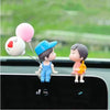 A cute couple figurine with a balloon is displayed on a car dashboard.