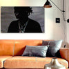 A dark portrait of a person with dreadlocks wearing a silver chain is displayed above an orange leather sofa.