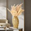 A golden wrinkle ceramic tabletop vase filled with dried grasses and flowers sits on a glass table.