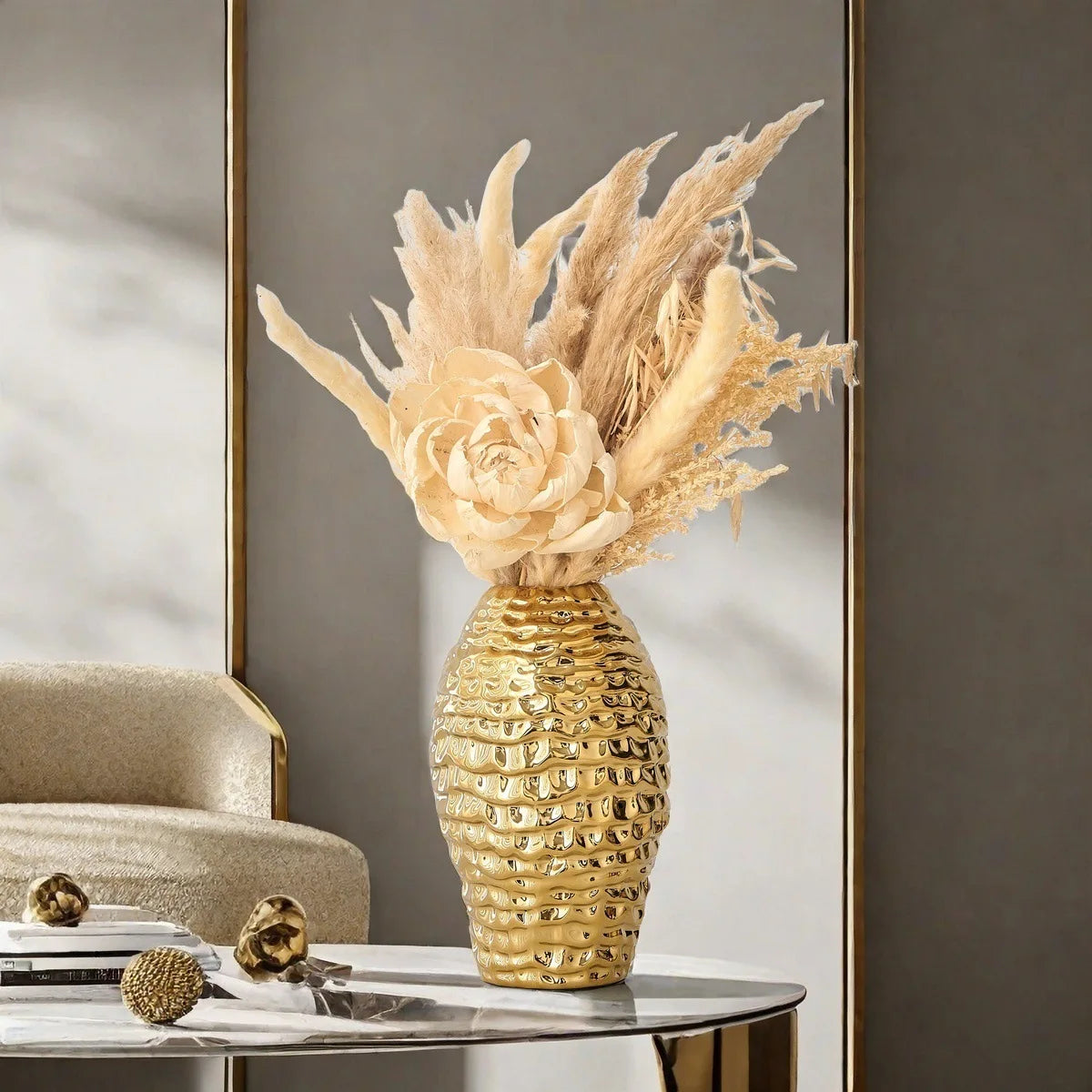 A golden wrinkle ceramic tabletop vase filled with dried grasses and flowers sits on a glass table.