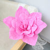 A large, vibrant pink foam rose flower is displayed on a light-colored surface.