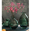 A set of three dark green glass mini vases with pink flowers displayed on a dark surface.
