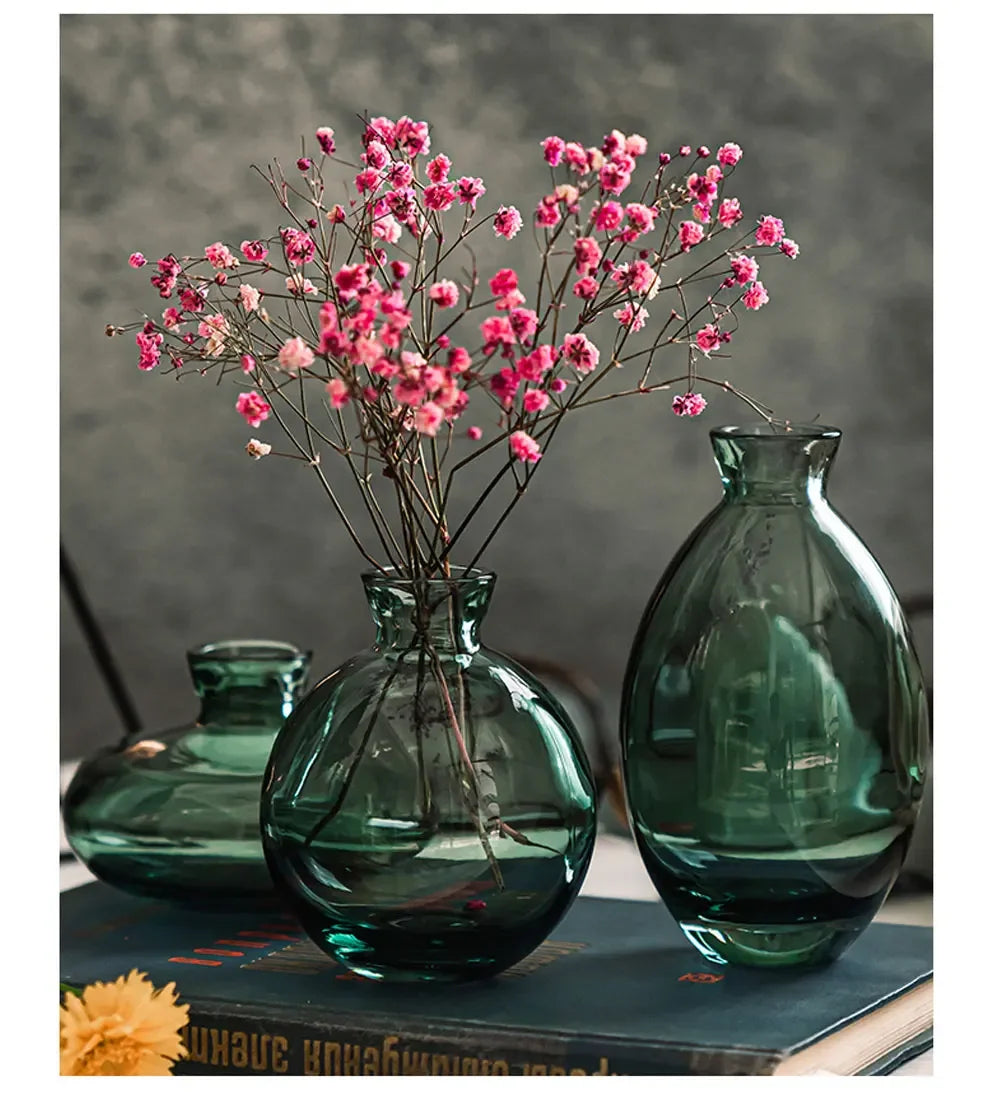 A set of three dark green glass mini vases with pink flowers displayed on a dark surface.