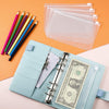 A light blue A6 PU leather budget planner binder with cash envelopes and expense sheets next to colored pencils and clear pla