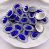 A pile of round and oval blue gemstones set in silver rhinestone flatbacks on a white plate.