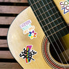 A close-up of a guitar body featuring colorful stickers that read Everyone Needs a Safe Space and Safe Space.