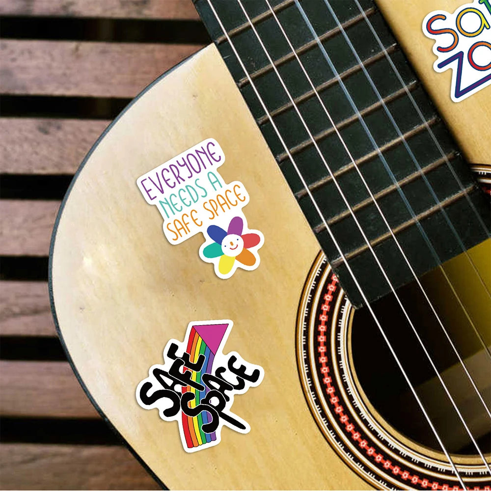 A close-up of a guitar body featuring colorful stickers that read Everyone Needs a Safe Space and Safe Space.