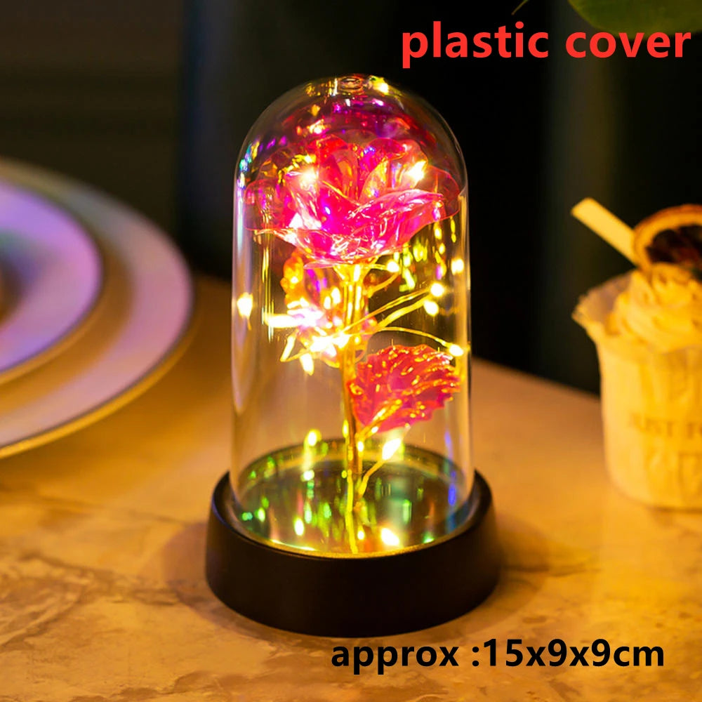 A glass dome containing an LED galaxy rose artificial flower illuminated with bright pink and yellow lights.