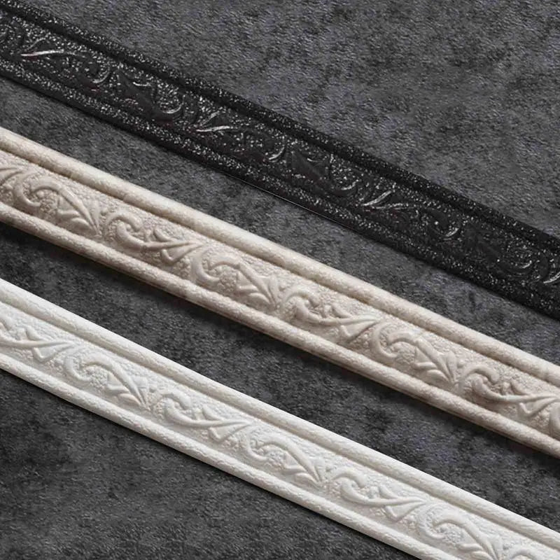 Three strips of white and black decorative corner wall trim strips laid diagonally on a dark gray textured surface.