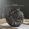 A dark gray resin vase with intricate swirling lines and textured surface, displayed on a wooden table.