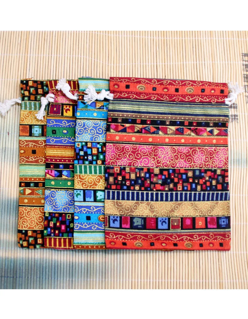 A collection of ten colorful vintage cotton drawstring gift pouches arranged horizontally on a light woven background.