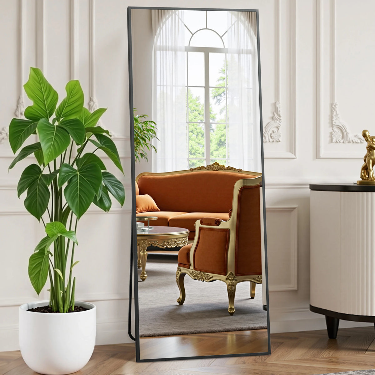 A full length body mirror with an aluminum frame reflecting a room interior and a large green plant.