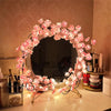 A circular wreath made of pink LED rattan string lights decorated with small flowers, displayed on a table.