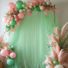 A soft pink and green tulle backdrop decorated with balloons and floral accents for an event.