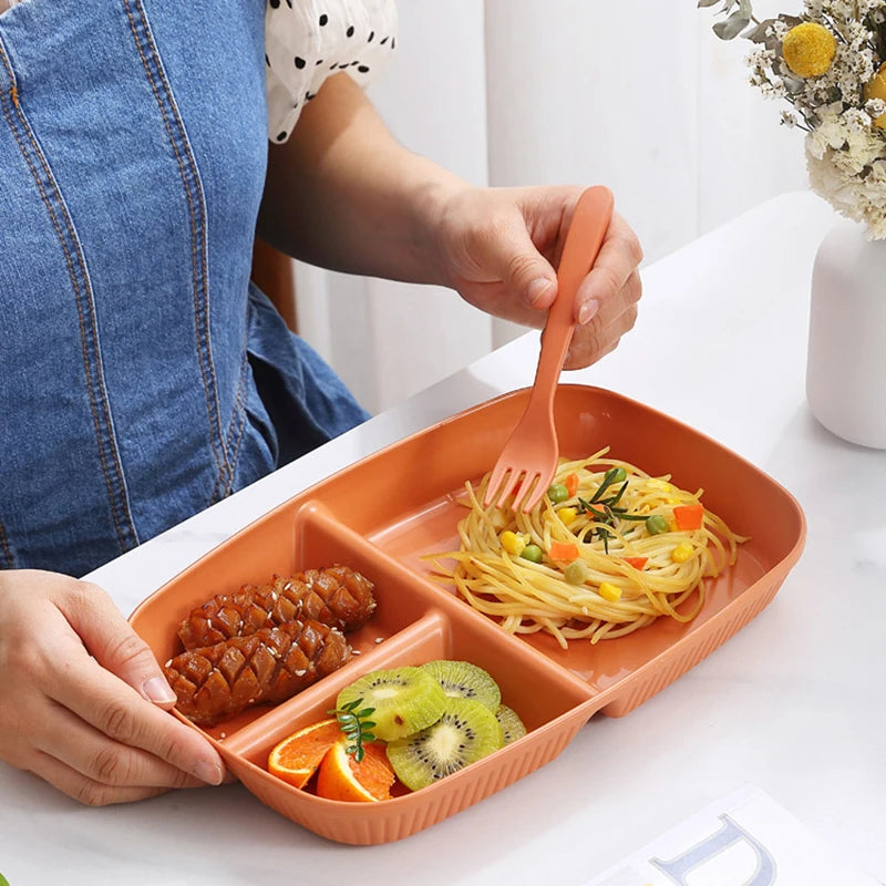 A person is holding an orange 3-compartment portion control plate filled with spaghetti and meat on a white table.
