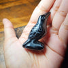 A handcrafted obsidian crow statue is held in a person's hand.