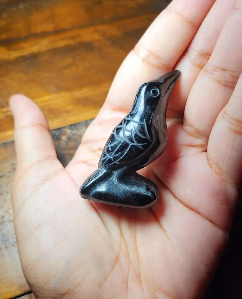 A handcrafted obsidian crow statue is held in a person's hand.