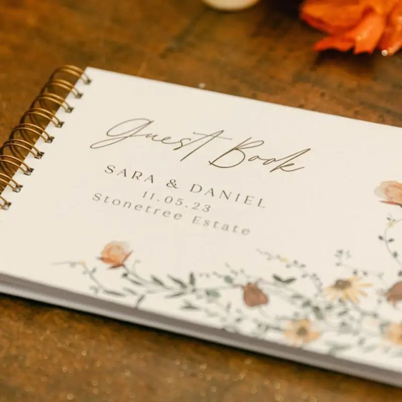 A personalized wedding guest book with gold lettering and floral accents resting on a wooden surface.