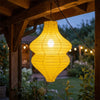 Linterna de flor vintage artesanal amarilla brillante colgando en una pérgola de madera al anochecer.