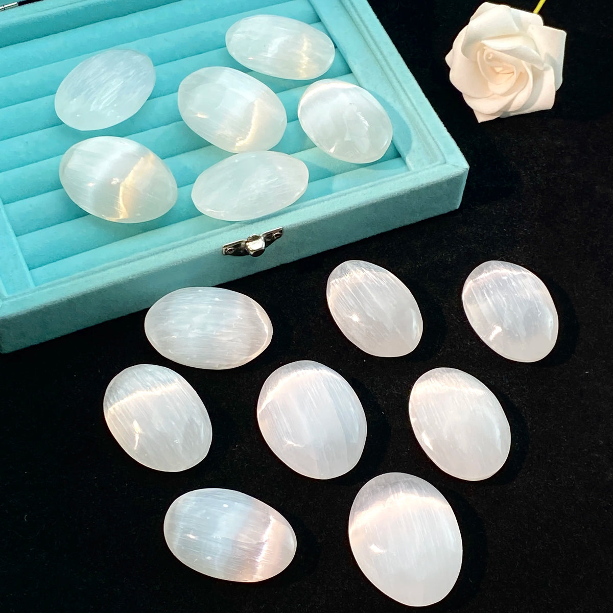 A collection of oval, translucent white selenite palm crystals displayed in a light blue wooden tray.