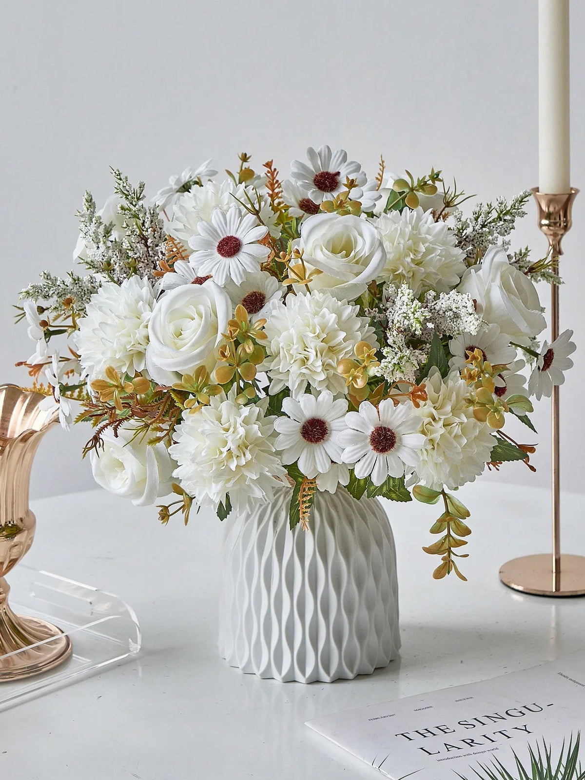 A bouquet of white artificial silk flowers featuring roses, daisies, and greenery displayed in a white vase.