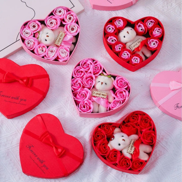 A collection of pink and red heart-shaped gift boxes filled with rose flowers and white bear soaps.
