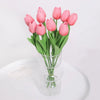 A bouquet of pink artificial tulip flowers in a clear glass vase on a white surface.