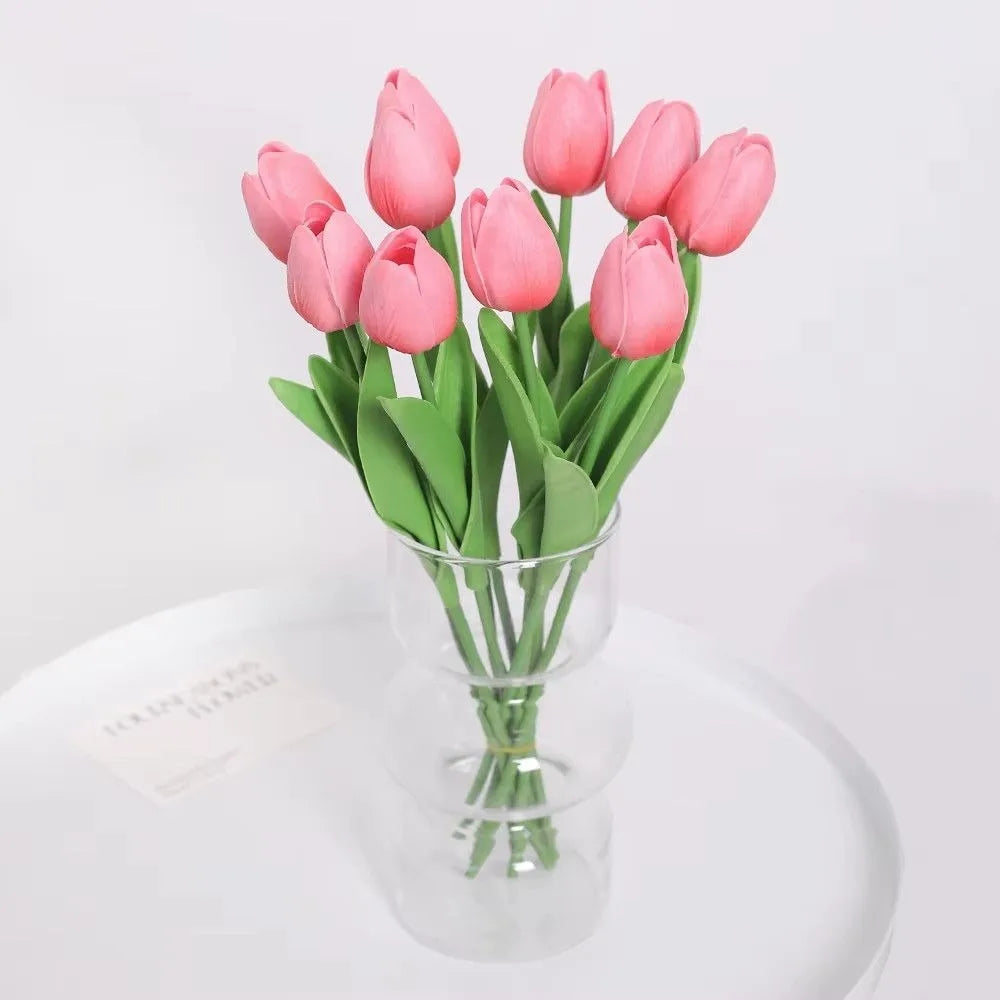 A bouquet of pink artificial tulip flowers in a clear glass vase on a white surface.
