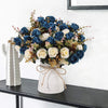A bouquet of artificial silk roses in shades of blue, cream, and muted green arranged in a white vase.