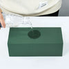 A hand pours water from a plastic bottle onto a dark green foam block for party decor.