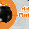 A black plastic witch cauldron mug filled with Halloween treats is being held over an orange plate.